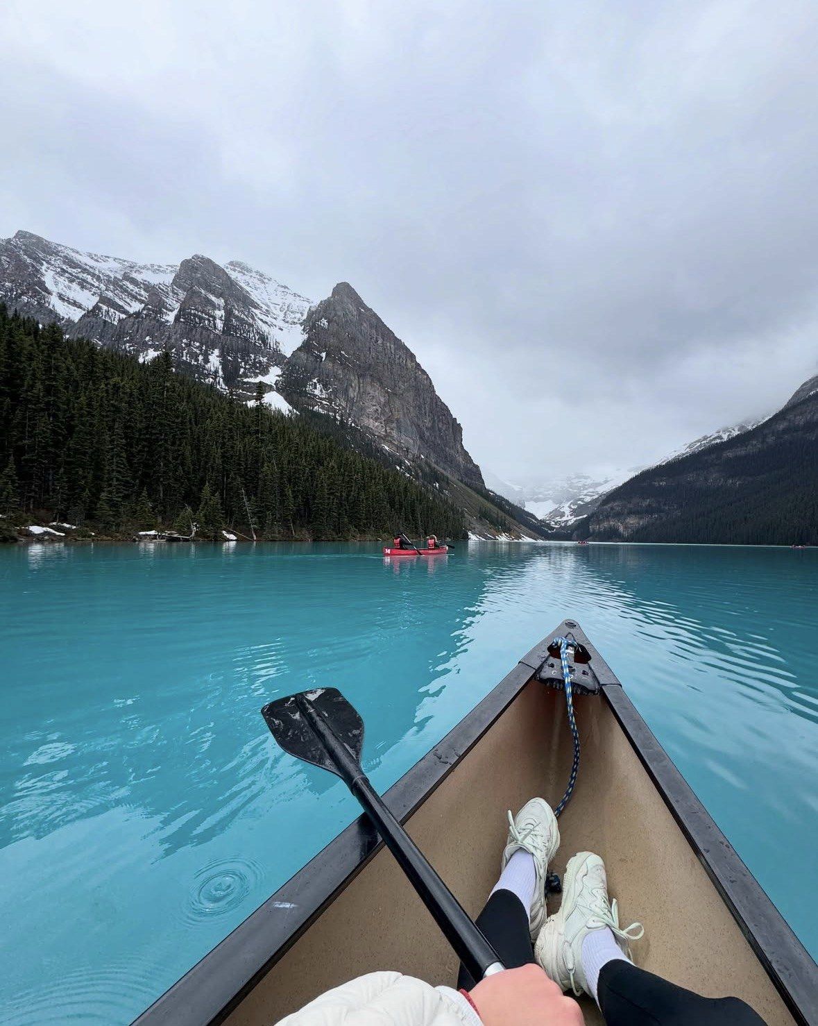 Paddler's view from a canoe bow across Lake Louise toward cloudy summits