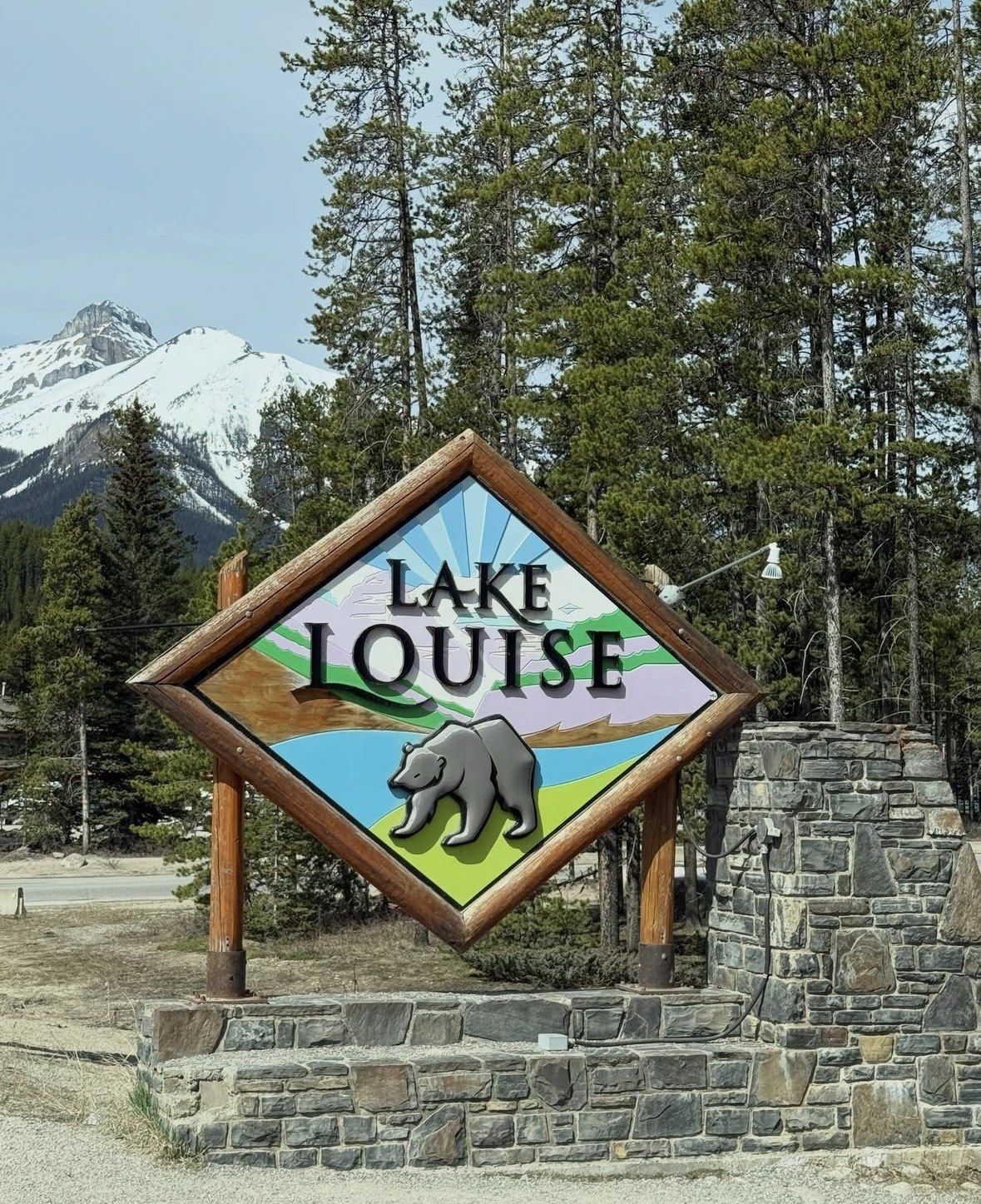 Carved Lake Louise village sign with bear painting below snowy peaks