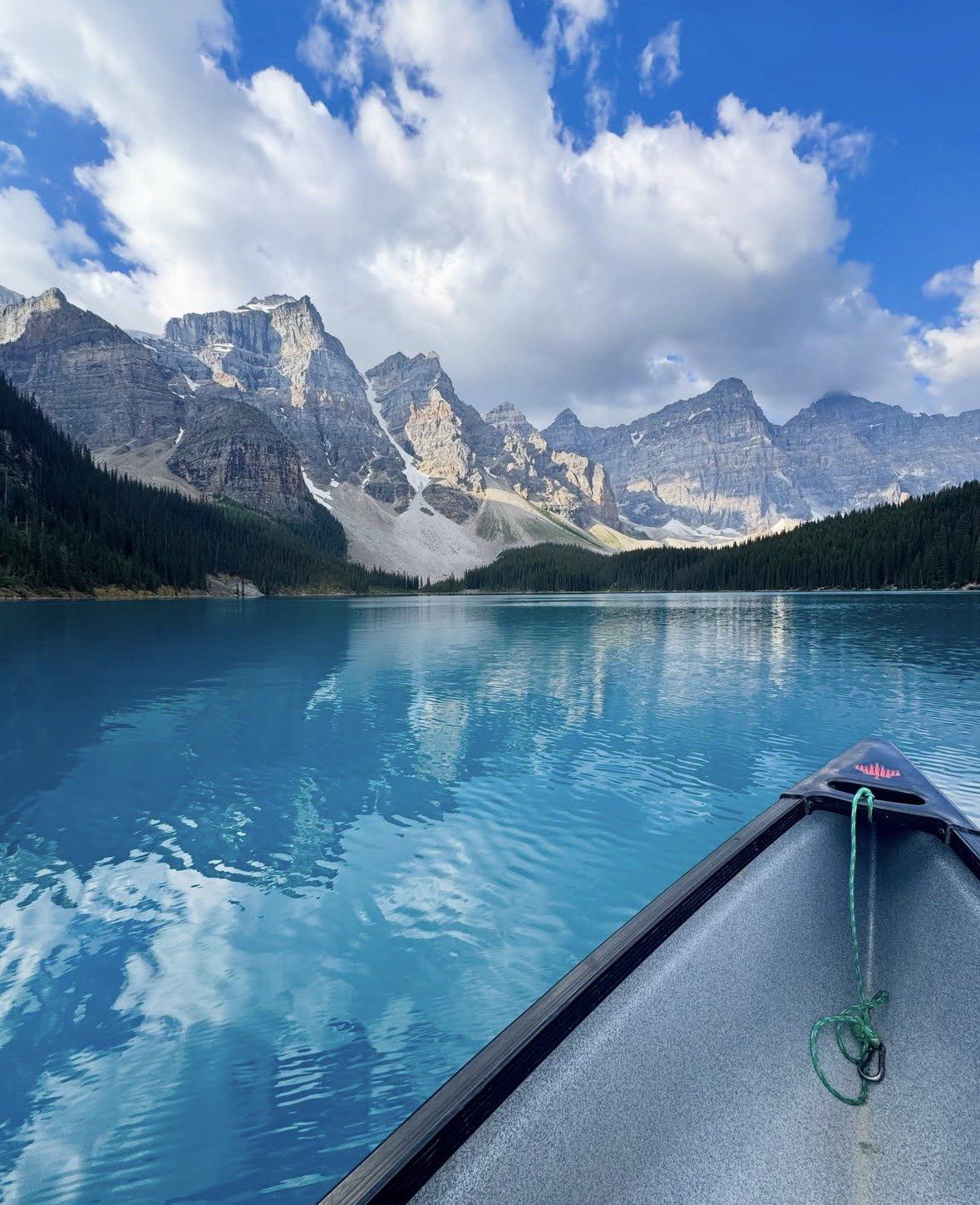 Canoe bow pointing toward jagged peaks reflected in blue summer water