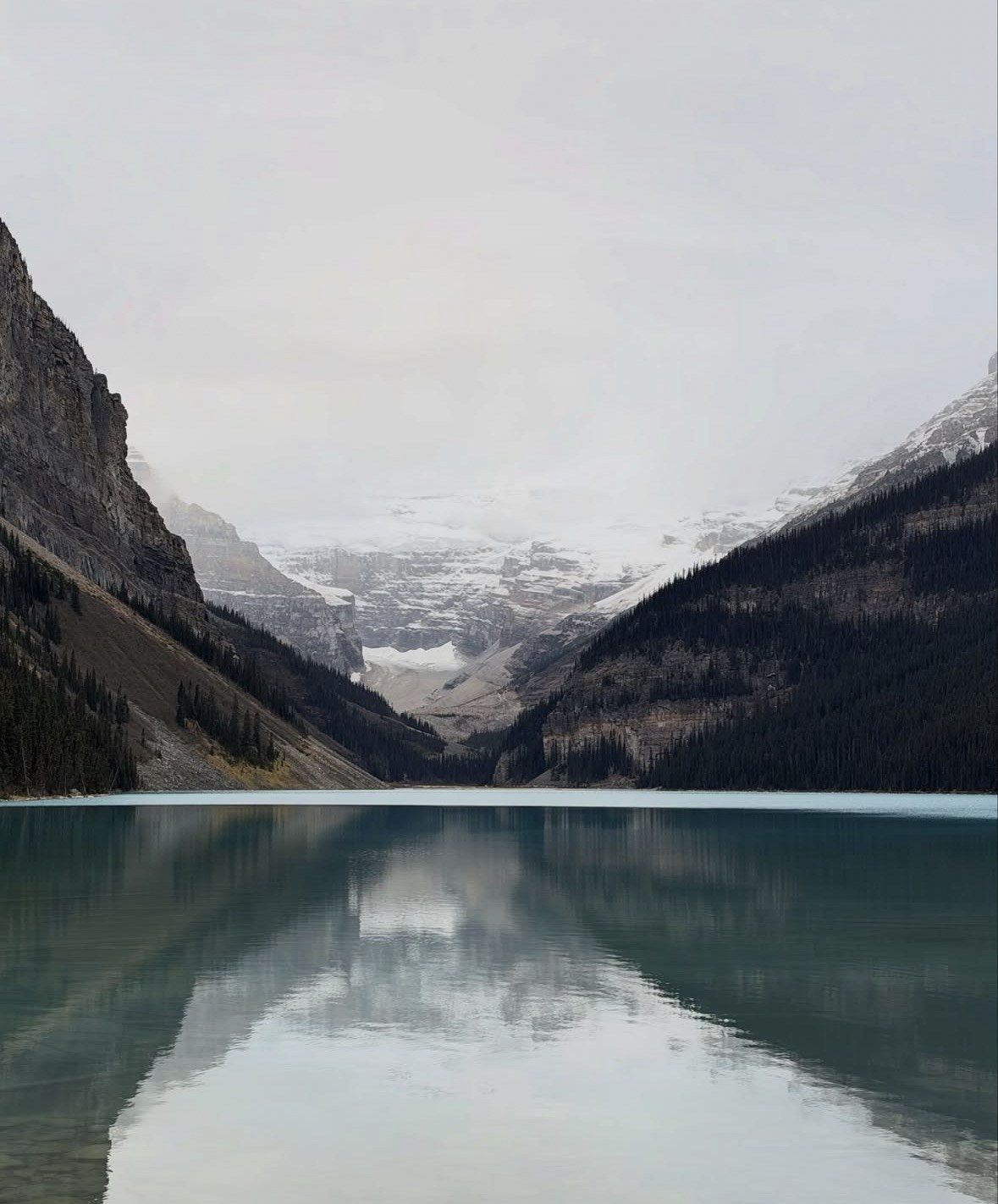 Victoria Glacier under low grey cloud reflected in still Lake Louise